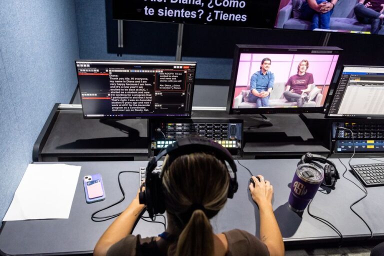 Back view of a technician with headphones operating a broadcast console, with computer screens displaying software interface and a live feed of two individuals discussing on a TV show, representing Lifelong Learning at ACC.